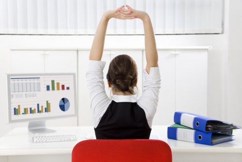 Rear view of young businesswoman sitting at desk stretching. Copy space