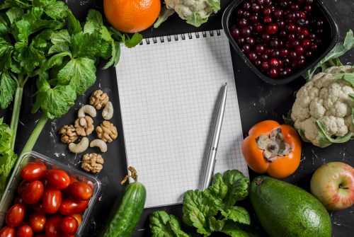 Food background. Fresh vegetables, fruits and blank notepad on a dark background. Concept of healthy eating, diet and planning